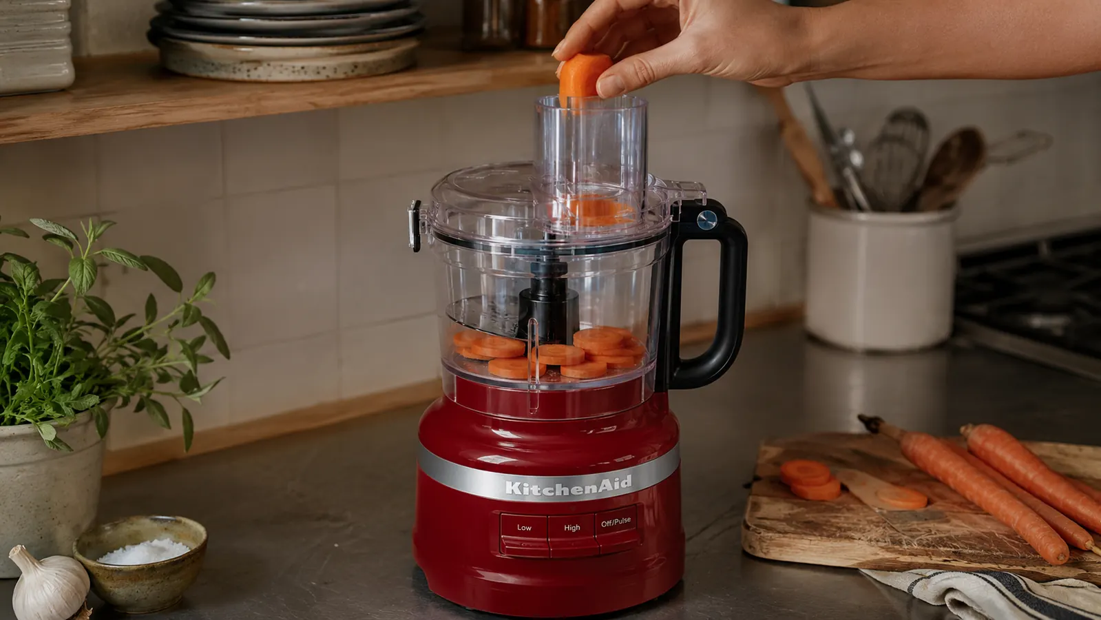 A hand feeding sliced carrots into the food processor's feed tube