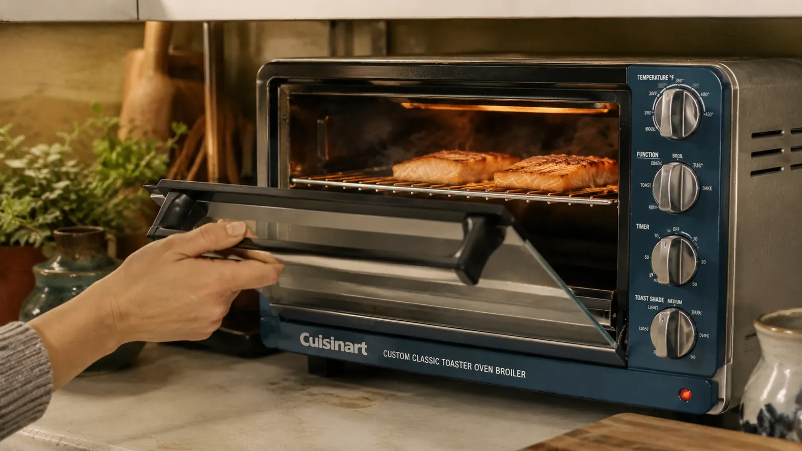 A hand opening the toaster oven broiler door and checking salmon fillets under the top element