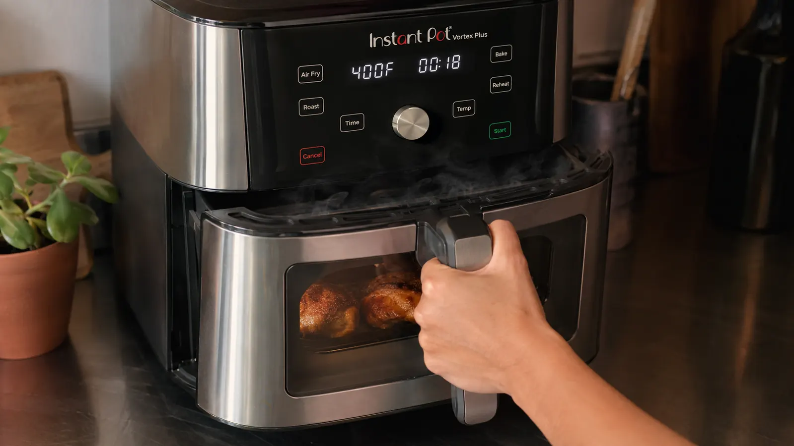 A hand opening the air fryer drawer to check crispy chicken thighs through the clear window