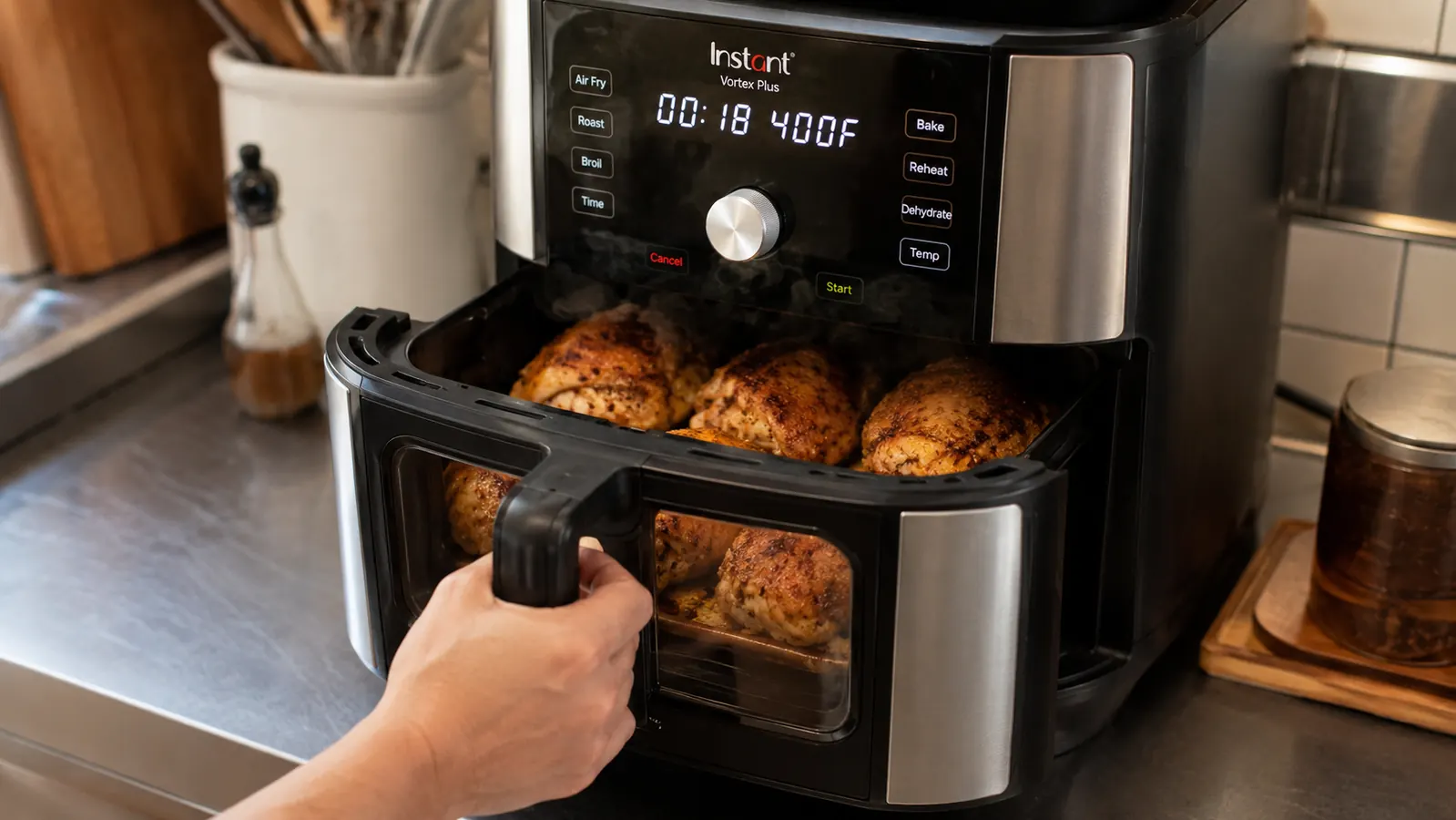 A hand pulling open the Instant Pot Vortex Plus drawer to check chicken thighs through the clear window
