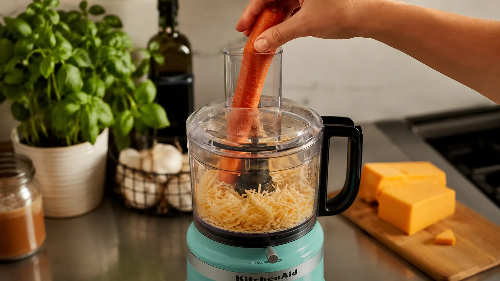 A hand feeding a carrot through the narrow opening of the two-in-one feed tube while the processor runs