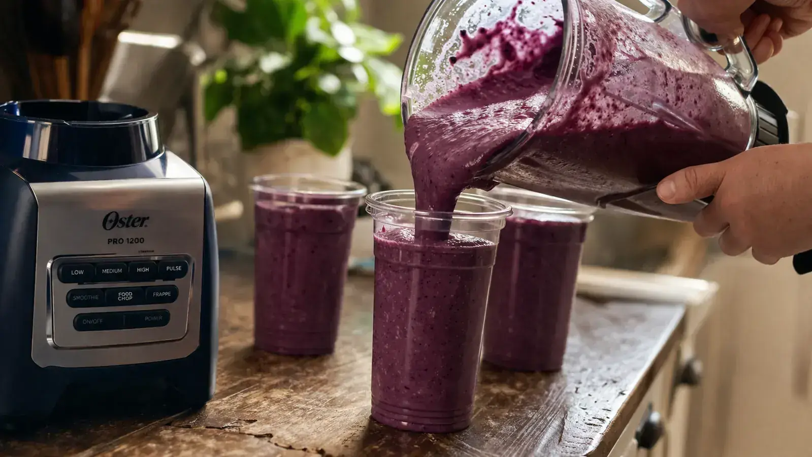 A hand pouring a purple spinach and berry smoothie from a full-size blender jar into a to-go cup on a narrow kitchen counter